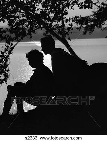 1920S Silhouette Of Couple Sitting On Rock Under Tree Lakeside View Large Photo Image Stock Image - 1920S Silhouette Of Couple Sitting On Rock Under Tree Lakeside . Fotosearch
