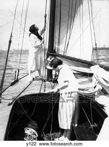 1920S Two Women On Deck Of Catboat One In Cockpit Pulling Ropes Other Standing By Main Mast Pulling Rope To Raise Main Sail View Large Photo Image Stock Image - 1920S Two Women On Deck Of Catboat One In Cockpit Pulling Ropes Other Standing By Main Mast Pulling Rope To Raise Main Sail. Fotosearch
