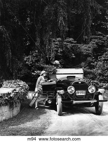 Picture - 1920S Woman Getting Into Passenger Side Of Car Carrying Golf Bag In Wooded Area . Fotosearch