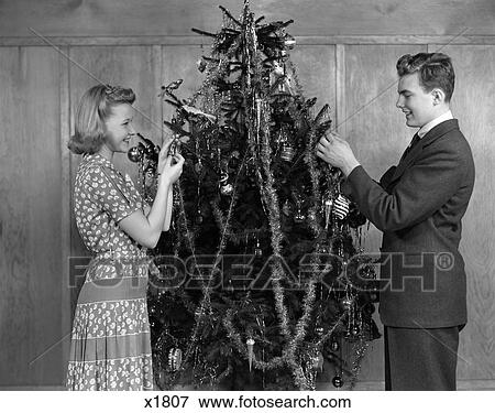 1930 1930S 1940 1940S Couple Decorating Christmas Tree With Tinsel And Ornaments View Large Photo Image Stock Photo - 1930 1930S 1940 1940S Couple Decorating Christmas Tree With Tinsel And Ornaments . Fotosearch