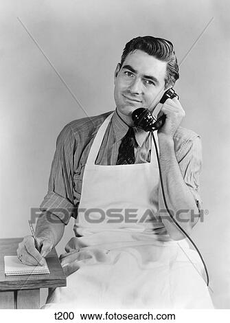 Stock Image - 1930 1930S 1940 1940S Man Wearing Apron Talking On Telephone Wtiting Down Order. Fotosearch