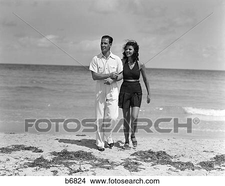 1930 1930S Couple Arm In Arm Walking Up From Ocean Smiling Man In White Shirt & Slacks Woman In Dark Halter Top & Shorts View Large Photo Image Picture - 1930 1930S Couple Arm In Arm Walking Up From Ocean Smiling Man In White Shirt & Slacks Woman In Dark Halter Top & Shorts. Fotosearch