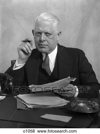 1930 1930S Man In Office Sitting At Desk Holding Papers Smoking A Cigar View Large Photo Image Stock Photo - 1930 1930S Man In Office Sitting At Desk Holding Papers Smoking A Cigar . Fotosearch