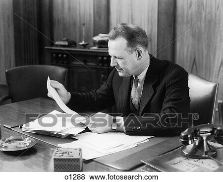 1930 1930S Man Sitting At Desk In Office Looking Through Papers View Large Photo Image Stock Photo - 1930 1930S Man Sitting At Desk In Office Looking Through Papers. Fotosearch