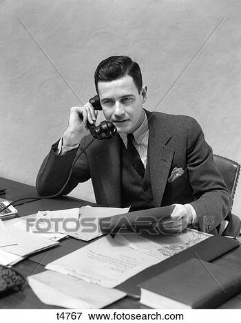 1930 1930S Man Sitting At Desk Looking At Papers Talking On Telephone View Large Photo Image Stock Photo - 1930 1930S Man Sitting At Desk Looking At Papers Talking On Telephone . Fotosearch