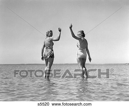 1930 1930S Two Girls Standing In Water Wearing Bathing Suits Looking Back Waving View Large Photo Image Stock Image - 1930 1930S Two Girls Standing In Water Wearing Bathing Suits Looking Back Waving . Fotosearch