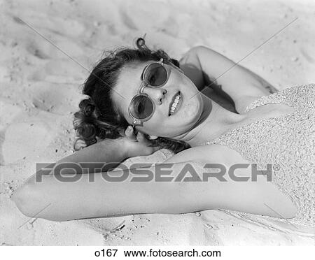 Stock Photo - 1930 1930S Woman In Sunglasses Lying On Beach Wearing Bathing Suit . Fotosearch