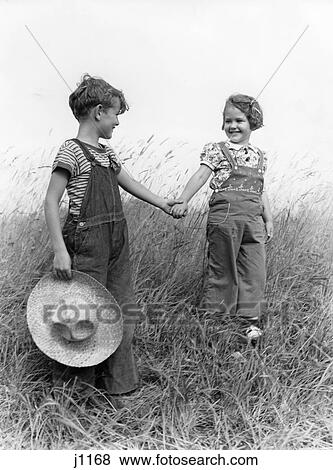 1930S 1940S Boy Girl Holding Hands Walk Down Grassy Hill Wearing Overalls Carrying Straw Hat View Large Photo Image Stock Photo - 1930S 1940S Boy Girl Holding Hands Walk Down Grassy Hill Wearing Overalls Carrying Straw Hat. Fotosearch