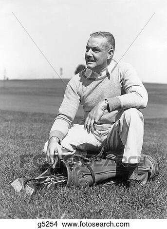 1930S 1940S Middle Age Man Kneeling In Grass With Hand Resting On Golf Bag & Clubs View Large Photo Image Picture - 1930S 1940S Middle Age Man Kneeling In Grass With Hand Resting On Golf Bag & Clubs . Fotosearch