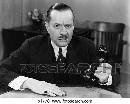 1930S 1940S Portrait Of Business Man Sitting At Office Desk Holding Phone In One Hand Serious Facial Expression Moustache View Large Photo Image Stock Photo - 1930S 1940S Portrait Of Business Man Sitting At Office Desk Holding Phone In One Hand Serious Facial Expression Moustache. Fotosearch