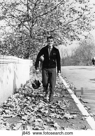 1930S 1940S Smiling Boy Walking Autumn Street Home From School Carrying Helmet And Football View Large Photo Image Stock Photography - 1930S 1940S Smiling Boy Walking Autumn Street Home From School Carrying Helmet And Football. Fotosearch