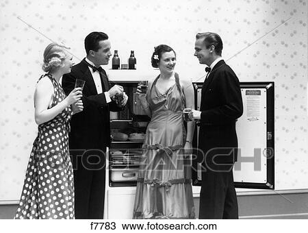 Stock Image - 1930S 1940S Two Couples Formally Dressed Standing In Front Of Refrigerator With Doors Open Drinking Beer . Fotosearch