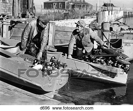 1930S 1940S Two Men Dressed For Duck Shooting Pushing Off From Shore In Two Small Boats Loaded With Duck Decoys Shotgun View Large Photo Image Stock Photograph - 1930S 1940S Two Men Dressed For Duck Shooting Pushing Off From Shore In Two Small Boats Loaded With Duck Decoys Shotgun. Fotosearch