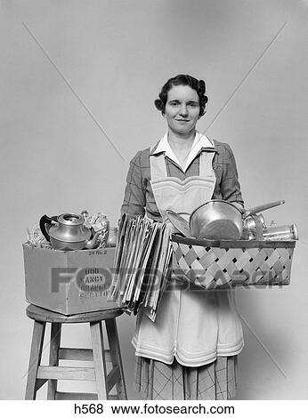 1930S 1940S Woman Housewife Facing Camera Holding Basket Filled With Pots Pans Cookware Chore Apron View Large Photo Image Stock Photo - 1930S 1940S Woman Housewife Facing Camera Holding Basket Filled With Pots Pans Cookware Chore Apron . Fotosearch