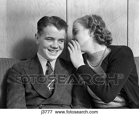 1930S 1940S Young Couple Teen Sitting Couch Girl Whispering Secret Into Boys Ear View Large Photo Image Stock Photo - 1930S 1940S Young Couple Teen Sitting Couch Girl Whispering Secret Into Boys Ear . Fotosearch