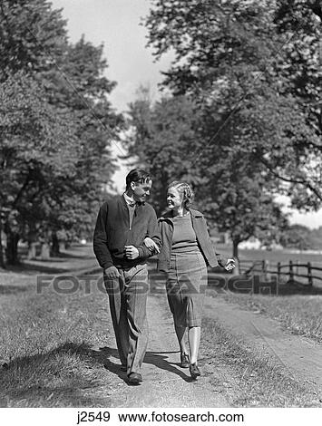 Stock Photo - 1930S 1940S Young Teen Couple Boy Girl Strolling Down Country Lane Arm In Arm . Fotosearch