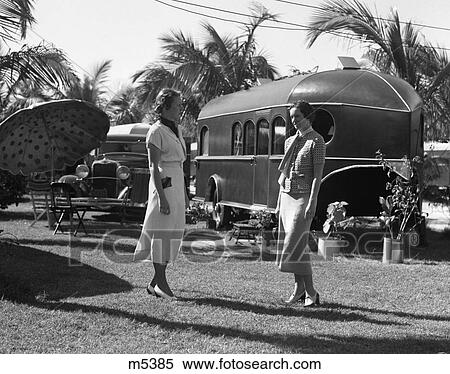 1930S 2 Women Standing Talking On Tropical Lawn In Florida Trailer Park With A Car Umbrella & Chairs View Large Photo Image Stock Photography - 1930S 2 Women Standing Talking On Tropical Lawn In Florida Trailer Park With A Car Umbrella & Chairs . Fotosearch