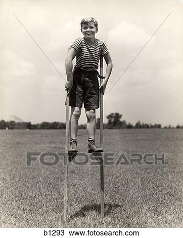 Stock Image -  1930S 940S Smiling Happy Boy Wearing Striped Shirt & Short Pants Walking On Pair Of Stilts . Fotosearch