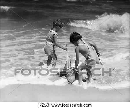 1930S Boy Girl Playing Ocean Surf Water Sailboat Shovel Pail Toys Seashore Vacation View Large Photo Image Stock Photo - 1930S Boy Girl Playing Ocean Surf Water Sailboat Shovel Pail Toys Seashore Vacation . Fotosearch