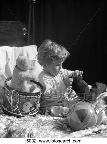 Stock Image - 1930S Boy In Bed With A Ball & Teddy Bear Sitting On A Toy Drum Wearing Pajamas Playing . Fotosearch