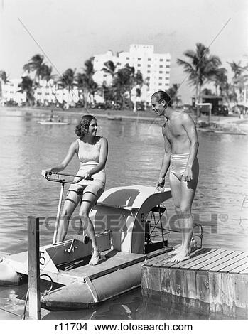 1930S Couple Man Woman Bathing Suit Suits Woman Sitting On Pedal Boat Man Standing On Dock View Large Photo Image Picture - 1930S Couple Man Woman Bathing Suit Suits Woman Sitting On Pedal Boat Man Standing On Dock . Fotosearch