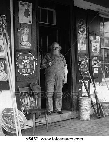 1930S Elderly Bearded Man In Overalls Smoking Pipe Standing In Doorway Of General Store View Large Photo Image Stock Image - 1930S Elderly Bearded Man In Overalls Smoking Pipe Standing In Doorway Of General Store . Fotosearch