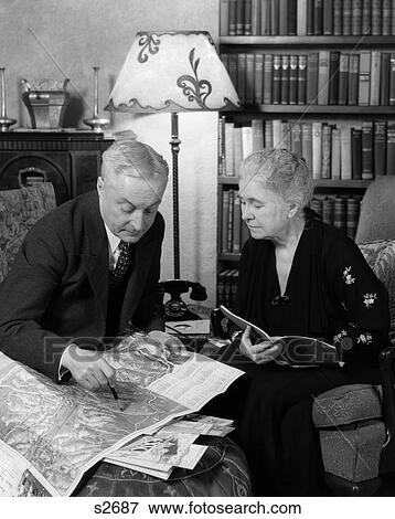 1930S Elderly Couple Man Woman Read Maps Books Travel Brochures Sit In Living Room Book Shelves View Large Photo Image Stock Photo - 1930S Elderly Couple Man Woman Read Maps Books Travel Brochures Sit In Living Room Book Shelves . Fotosearch