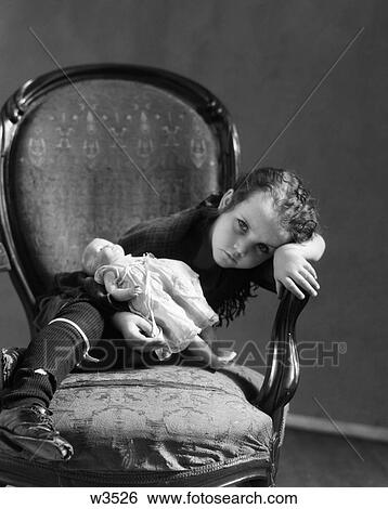 1930S Girl In Tattered Clothing Sitting Holding Baby Doll Leaning Head On Arm Of Chair With Sad Expression View Large Photo Image Stock Photograph - 1930S Girl In Tattered Clothing Sitting Holding Baby Doll Leaning Head On Arm Of Chair With Sad Expression . Fotosearch