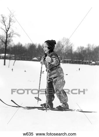 Stock Photography - 1930S Girl Wool Hat & Snowsuit On Cross Country Skis Holding Poles Skiing With Tree Line In The Distance Smiling Cold Fun Snow. Fotosearch