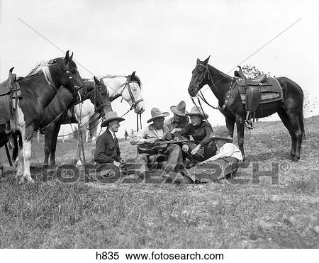 Stock Photography - 1930S Group Of Five Men Sitting By Their Horses One Man Holds Guitar Singing Country Western Music Cowboys Chaps Saddles Hats. Fotosearch