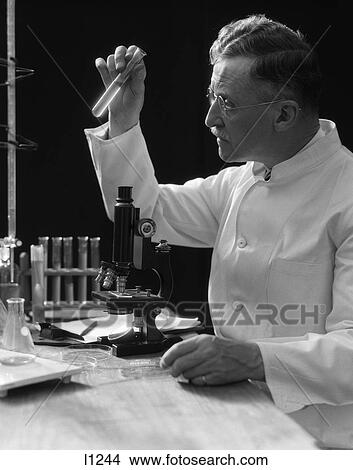1930S Lab Technician In White Coat Looking At Test-Tube In Front Of Microscope View Large Photo Image Picture - 1930S Lab Technician In White Coat Looking At Test-Tube In Front Of Microscope . Fotosearch