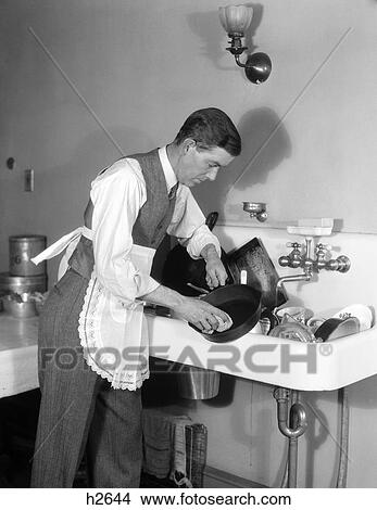 1930S Man Dressed In Shirt Tie Vest & Apron Bent Over A Sink Full Of Dishes Cleaning An Iron Skillet With A Dishcloth View Large Photo Image Picture - 1930S Man Dressed In Shirt Tie Vest & Apron Bent Over A Sink Full Of Dishes Cleaning An Iron Skillet With A Dishcloth . Fotosearch