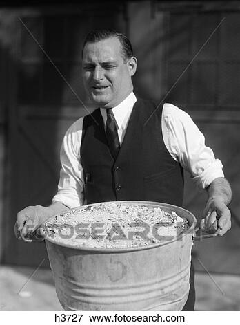 1930S Man In Shirt Vest & Tie Straining As He Carries A Heavy Ash Can Full Of Ashes View Large Photo Image Stock Photo - 1930S Man In Shirt Vest & Tie Straining As He Carries A Heavy Ash Can Full Of Ashes . Fotosearch