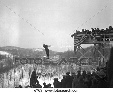 1930S Man Ski Jumping In Mid Air Crowd Spectators Grand Stand Draped With Flags And Bunting Winter Snowy Landscape View Large Photo Image Stock Image - 1930S Man Ski Jumping In Mid Air Crowd Spectators Grand Stand Draped With Flags And Bunting Winter Snowy Landscape . Fotosearch