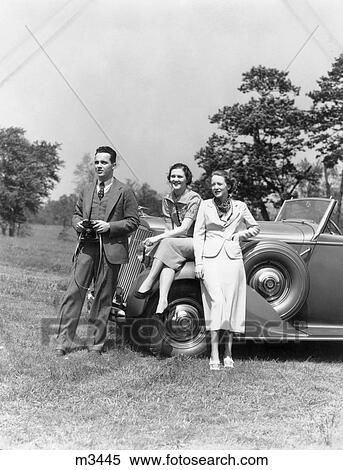 Stock Photography - 1930S Man With Camera And Two Women In Front Of Convertible Car Style Fashion Wealth Spectators . Fotosearch