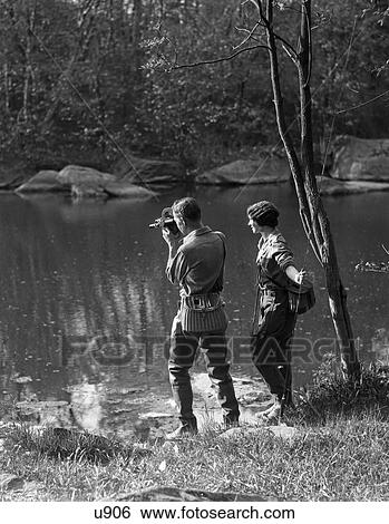 1930S Man With Camera & Woman With Trout Rod Both Are Wearing Waders & Wicker Creels View Large Photo Image Stock Photograph - 1930S Man With Camera & Woman With Trout Rod Both Are Wearing Waders & Wicker Creels. Fotosearch
