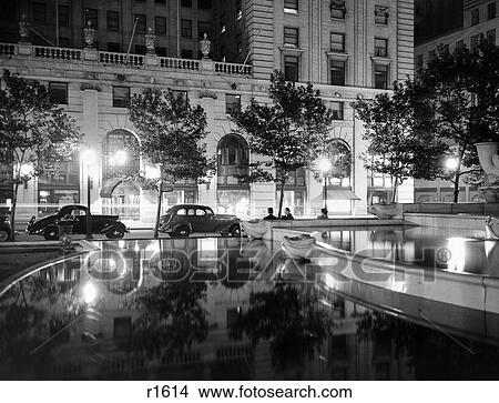 1930S Night Scene 5Th Avenue Hotel Front Tree Lined Sidewalk Motorcars Pool And Pedestrians Street Lamps Reflecting On Surfaces View Large Photo Image Picture - 1930S Night Scene 5Th Avenue Hotel Front Tree Lined Sidewalk Motorcars Pool And Pedestrians Street Lamps Reflecting On Surfaces. Fotosearch