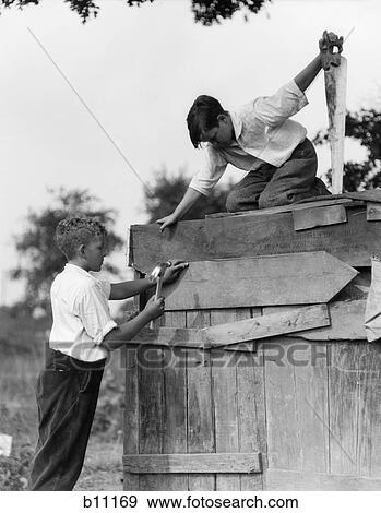 1930S Pair Of Boys Building Shack One Nailing Board To Side One On Roof With Saw View Large Photo Image Stock Photo - 1930S Pair Of Boys Building Shack One Nailing Board To Side One On Roof With Saw . Fotosearch