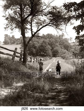 Stock Photograph - 1930S Rear View Of Boy & Girl In Straw Hats & Overalls Walking Down Farm Road With Dog Between Them . Fotosearch