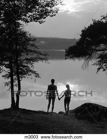 1930S Rear View Silhouette Of Man & Woman In Bathing Suits Holding Hands Watching Sunset Lakeside View Large Photo Image Stock Image - 1930S Rear View Silhouette Of Man & Woman In Bathing Suits Holding Hands Watching Sunset Lakeside . Fotosearch