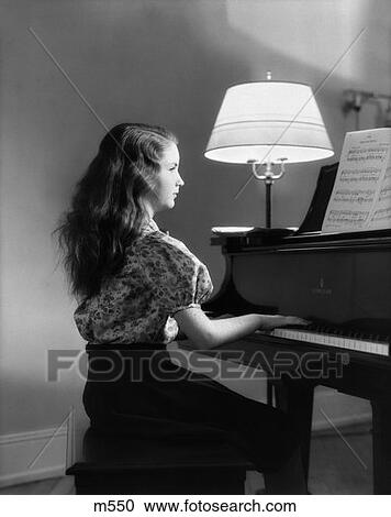 Stock Image - 1930S Side View Of Girl Playing Piano With Lamp Turned On Next To Her . Fotosearch