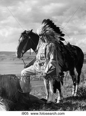 Stock Photography - 1930S Side View Of Sioux Indian Wearing Headdress Holding Reins Of Horse Next To Him . Fotosearch