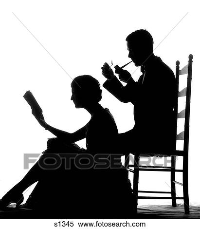 Stock Photography - 1930S Silhouette Of Man In Ladder-Back Chair Smoking Pipe With Woman Seated On Floor In Front Of Him Reading Book . Fotosearch