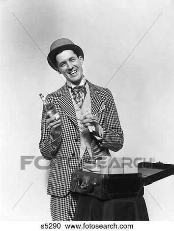 1930S Smiling Barker In Checkered Suit With Money In Hand Pointing To Bottle Of Tonic With Suitcase Open In Front Of Him View Large Photo Image Stock Image - 1930S Smiling Barker In Checkered Suit With Money In Hand Pointing To Bottle Of Tonic With Suitcase Open In Front Of Him . Fotosearch
