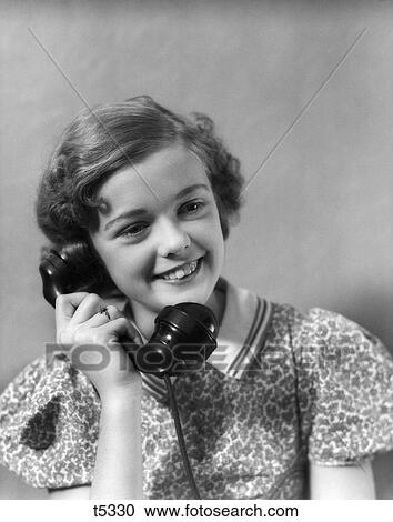 Stock Image - 1930S Teen Girl Smiling Brunette Print Dress Talking On Telephone Hand Held Black Receiver . Fotosearch