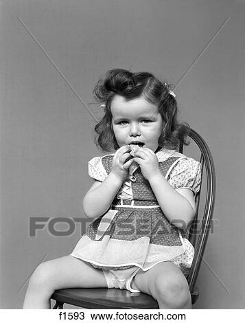 1930S Toddler Girl Sit In Wooden Chair Polka Dot Dress Showing Underpants Eating A Cookie With Both Hands Vintage Retro View Large Photo Image Stock Image - 1930S Toddler Girl Sit In Wooden Chair Polka Dot Dress Showing Underpants Eating A Cookie With Both Hands Vintage Retro. Fotosearch