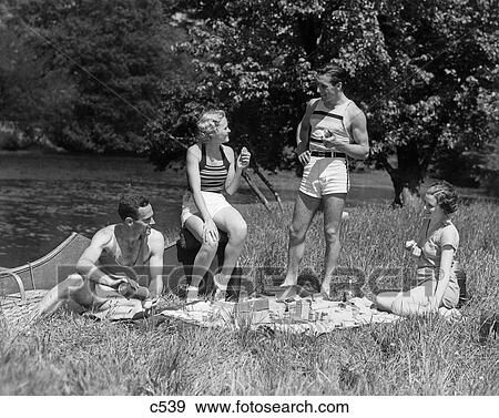 1930S Two Couples Having Summer Picnic With Food And Drink Spread Out On Blanket The Tip Of A Canoe Is Visible View Large Photo Image Stock Photo - 1930S Two Couples Having Summer Picnic With Food And Drink Spread Out On Blanket The Tip Of A Canoe Is Visible. Fotosearch