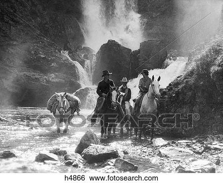 Stock Photograph - 1930S Two Men And Woman Riding Horseback With Fourth Horse Carrying Supplies In Stream . Fotosearch