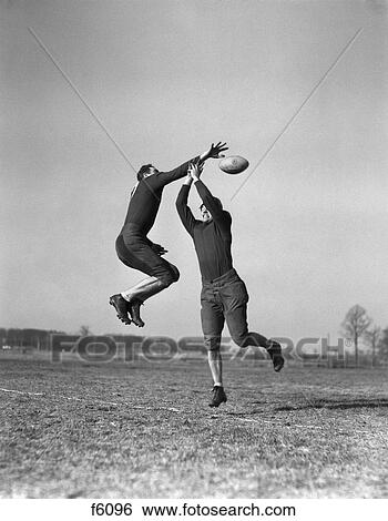 Stock Photograph - 1930S Two Men Jumping To Catch Football Not Wearing Helmets Practice . Fotosearch