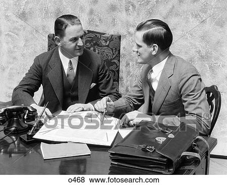 Stock Photo - 1930S Two Men Sitting On Same Side Of Office Desk Facing Each Other. Fotosearch